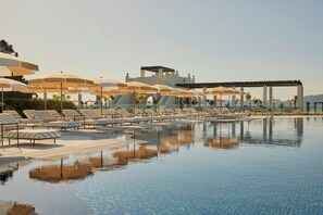 Un espace aménagé au bord de la piscine, avec des chaises longues et des parasols, une piscine à eau claire et un bâtiment au design moderne.