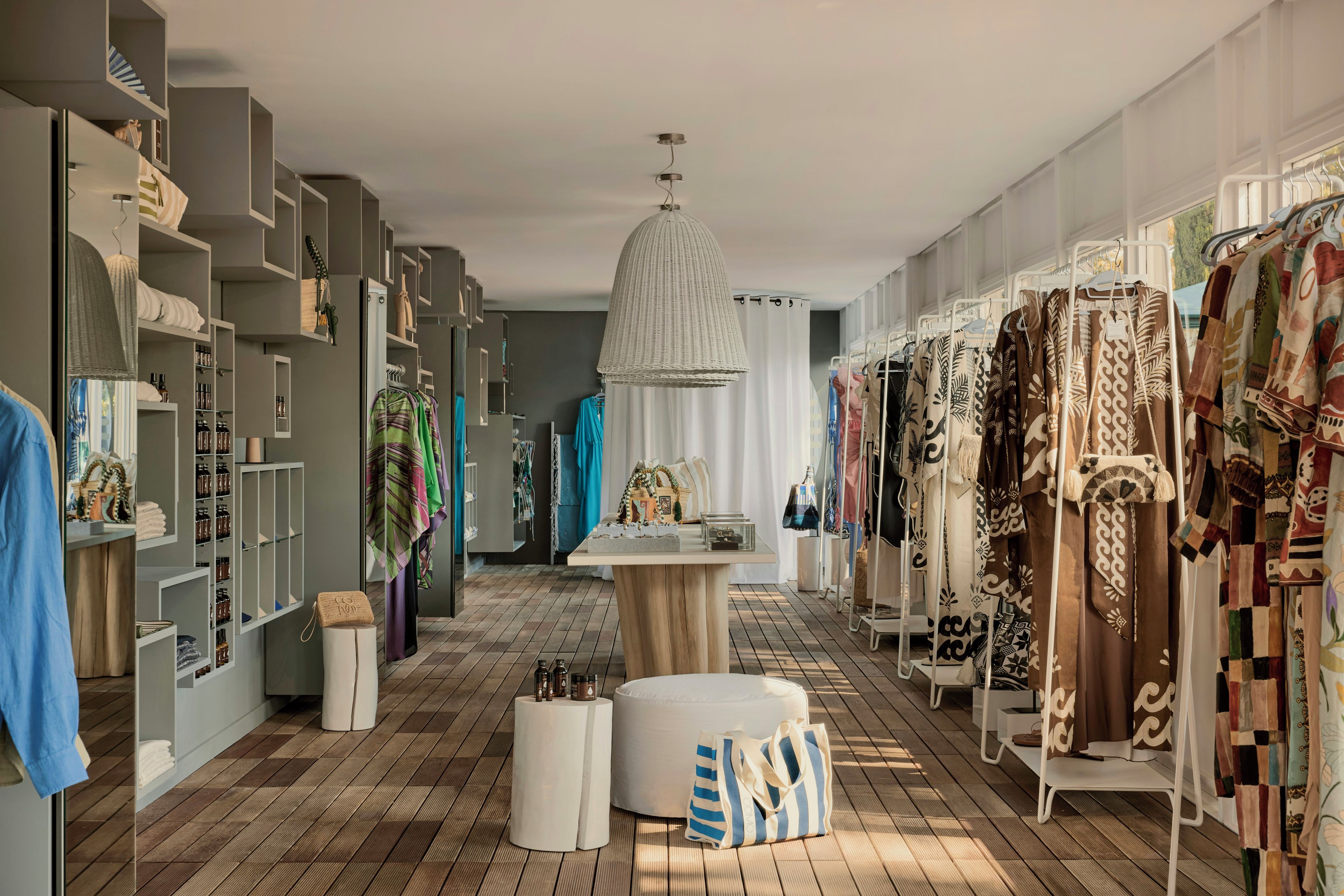 Habitación de hotel boutique con piso de madera, un otoman redondo en el centro, una lámpara colgante y un perchero con varias prendas.