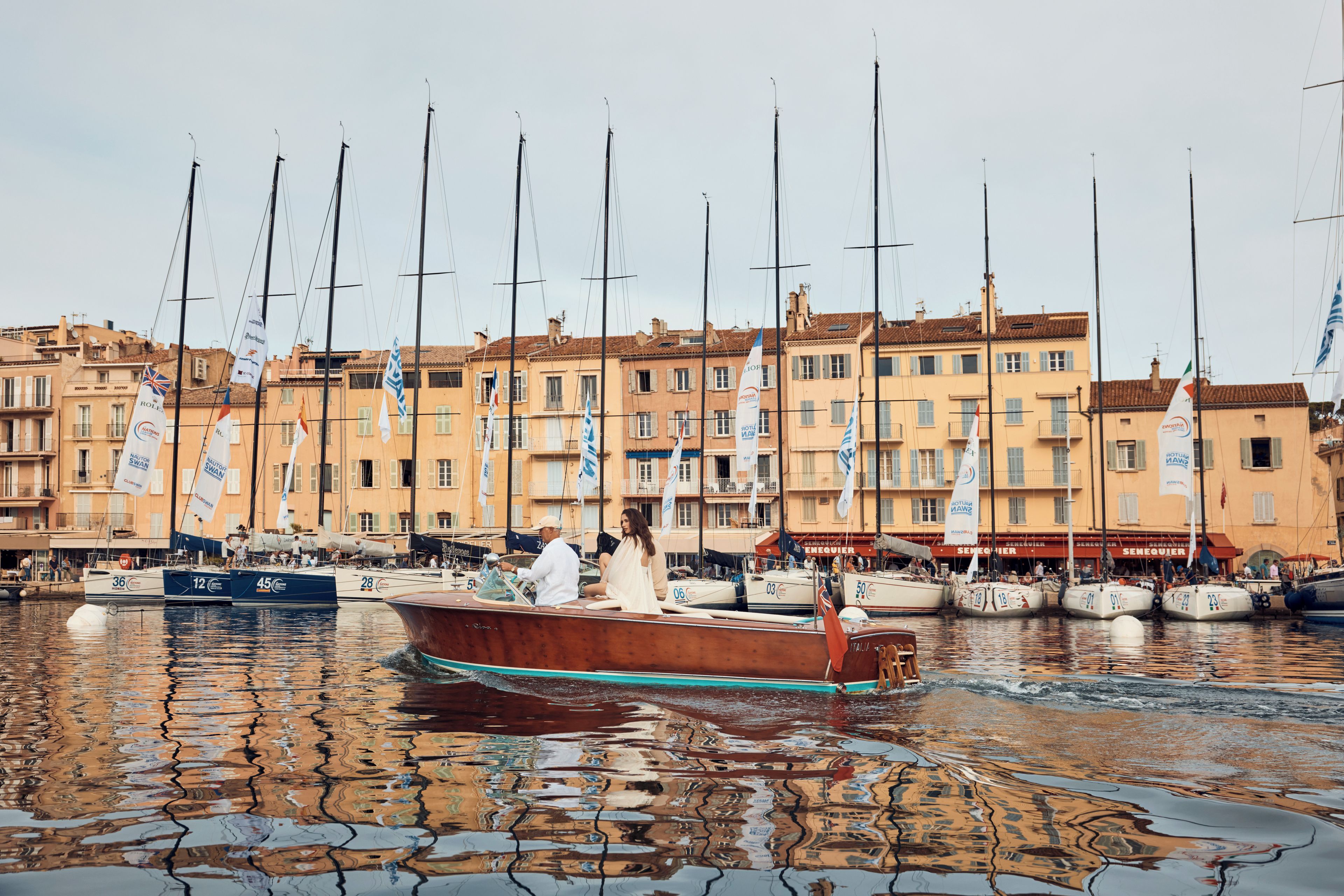 Un puerto deportivo con barcos amarrados, un bote de madera en primer plano y edificios con banderas al fondo.