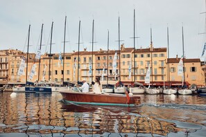 Un port de plaisance avec des bateaux amarrés, un bateau en bois au premier plan et des bâtiments avec des drapeaux en arrière-plan.