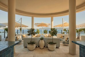 A covered outdoor seating area with a view of the sea, featuring potted plants, wicker furniture, and umbrellas. - COMO Le Beauvallon (Grimaud)