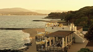 A seaside restaurant with outdoor seating overlooking the ocean, a wooden deck, and a view of the coastline. - COMO Le Beauvallon (Grimaud)