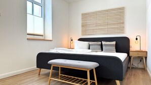 A modern bedroom with a dark-colored bed, wooden floor, and a window with blinds. - Harbor master Gunnar - Family-friendly retreat with balcony (Sassnitz)