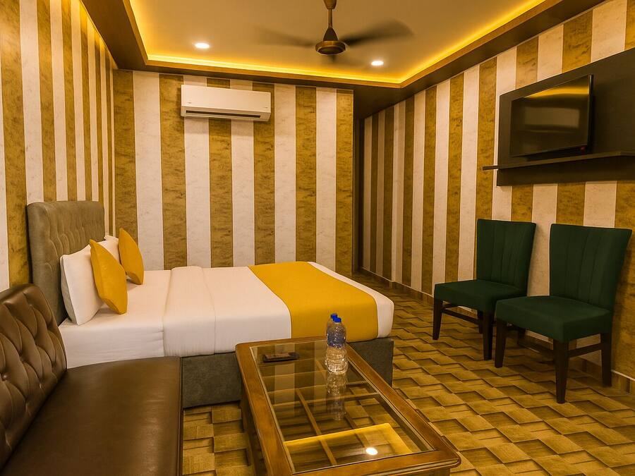 Habitación de hotel con cama, sofá, dos sillones, televisión y aire acondicionado.