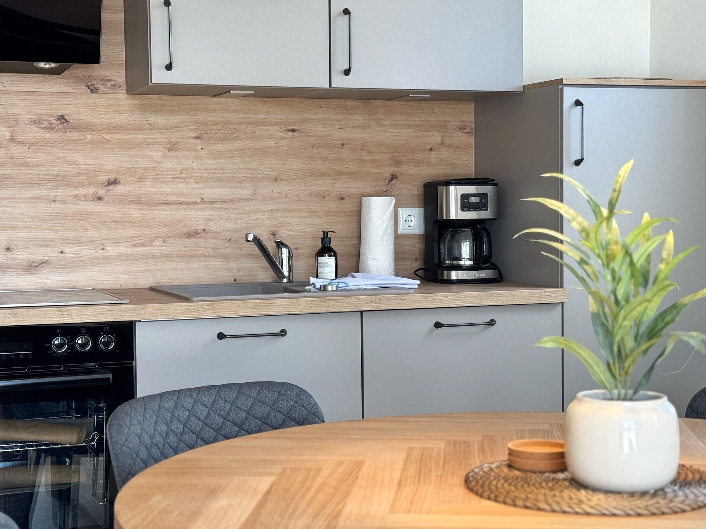 A modern kitchen with a wooden backsplash, a coffee maker, and a dining area with a round table and chairs.