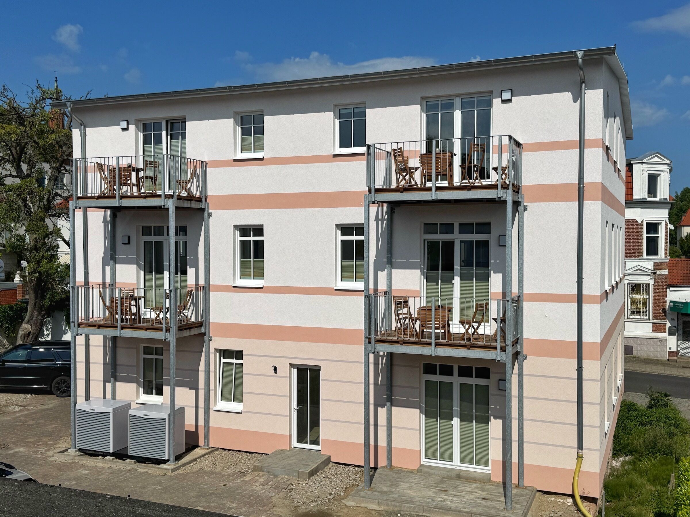 A multi-story building with balconies, a carport, and a small garden area.