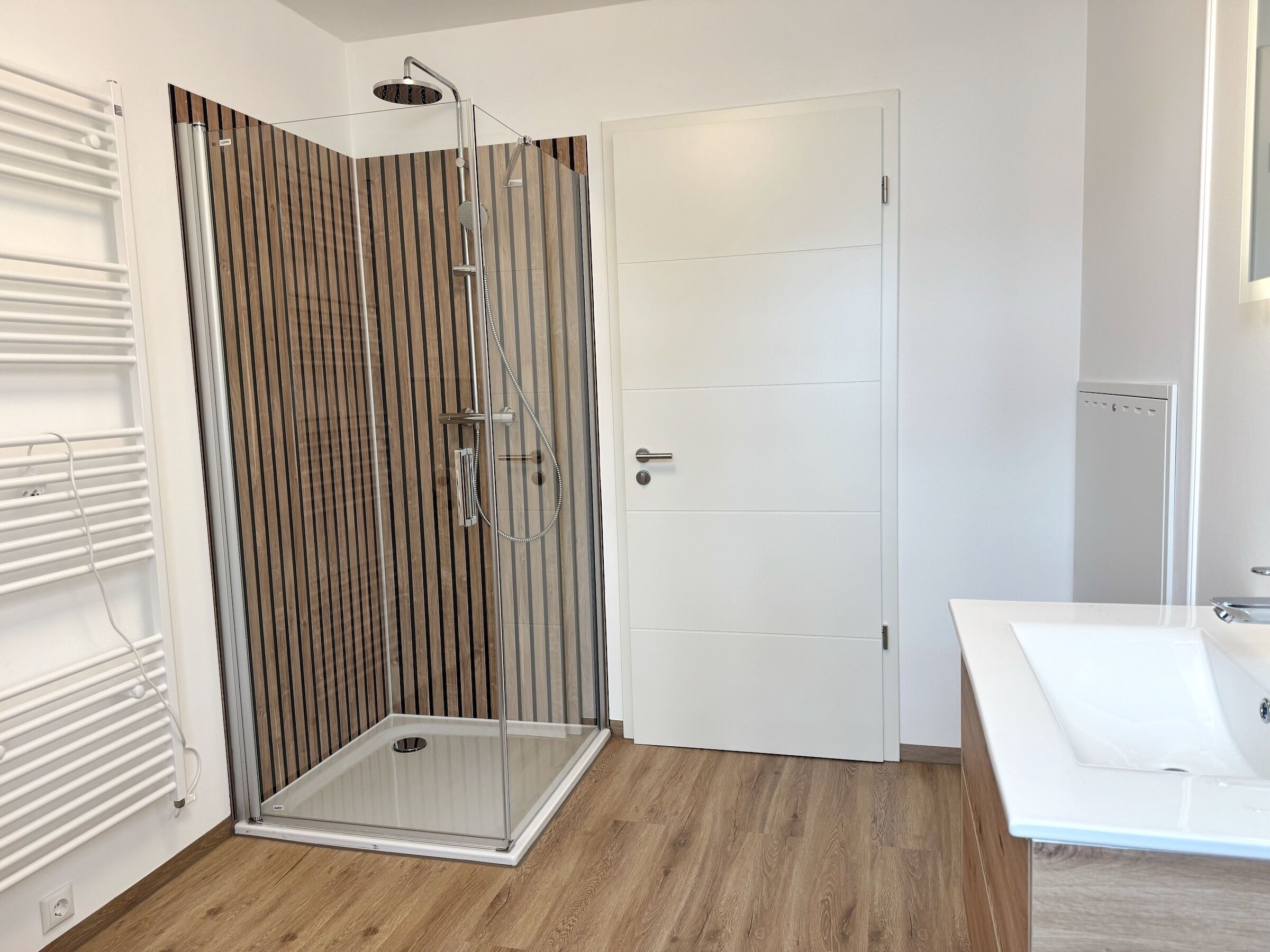 A modern bathroom with a glass shower enclosure, a white door, and a white bathtub.