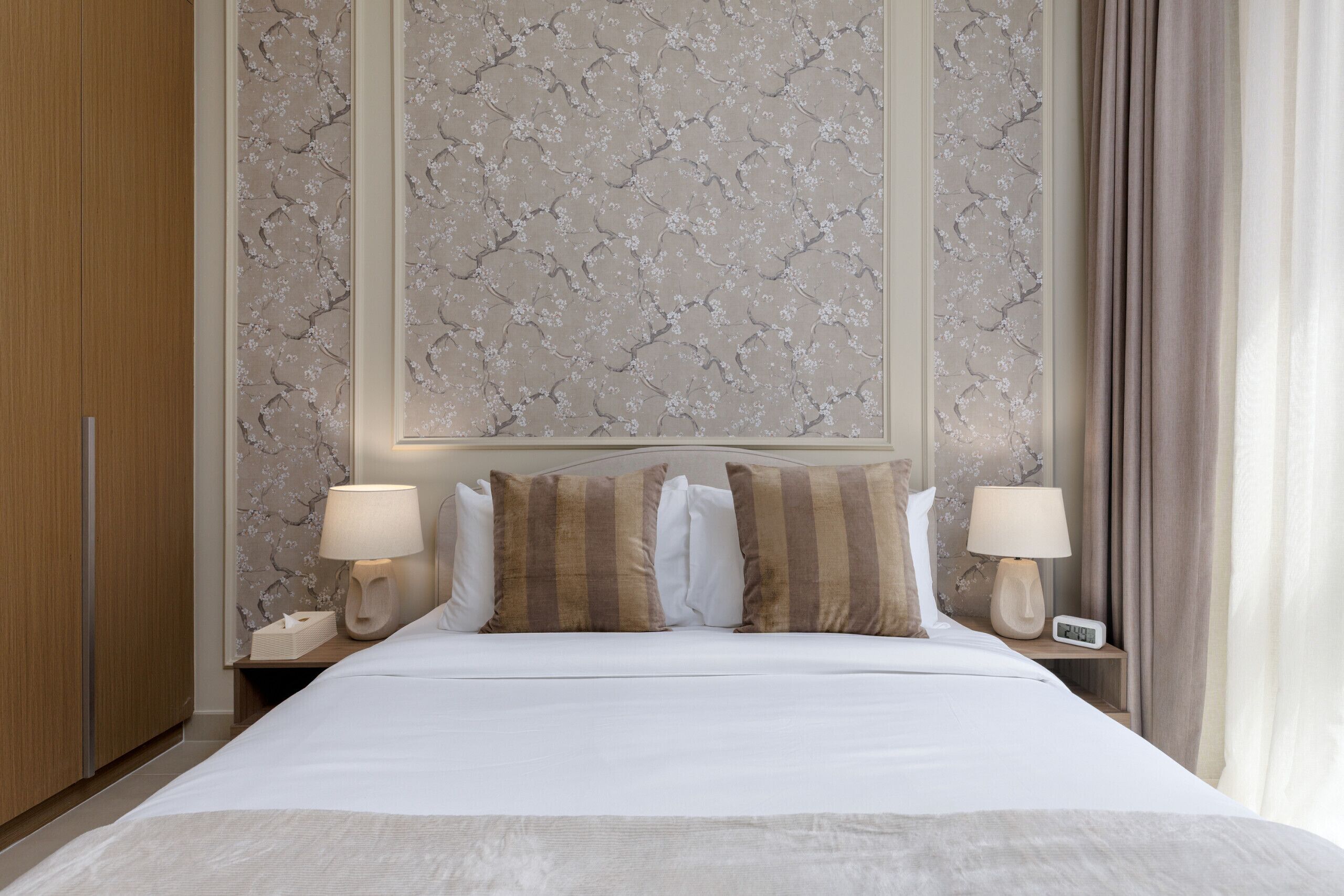Una camera d'albergo con un letto grande, due comodini con lampade, un tavolino e una parete con motivo floreale.