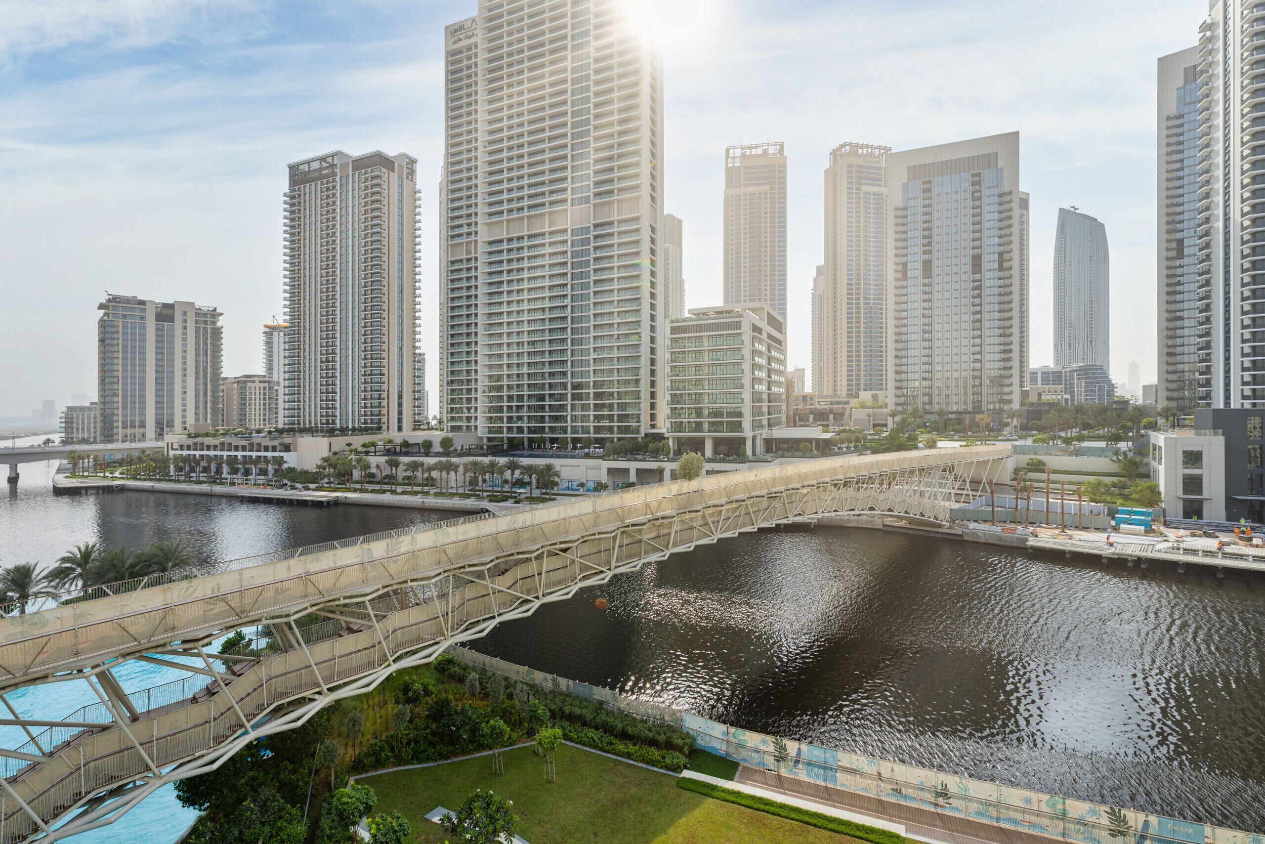 A modern urban waterfront with high-rise buildings, a pedestrian bridge, and a river.