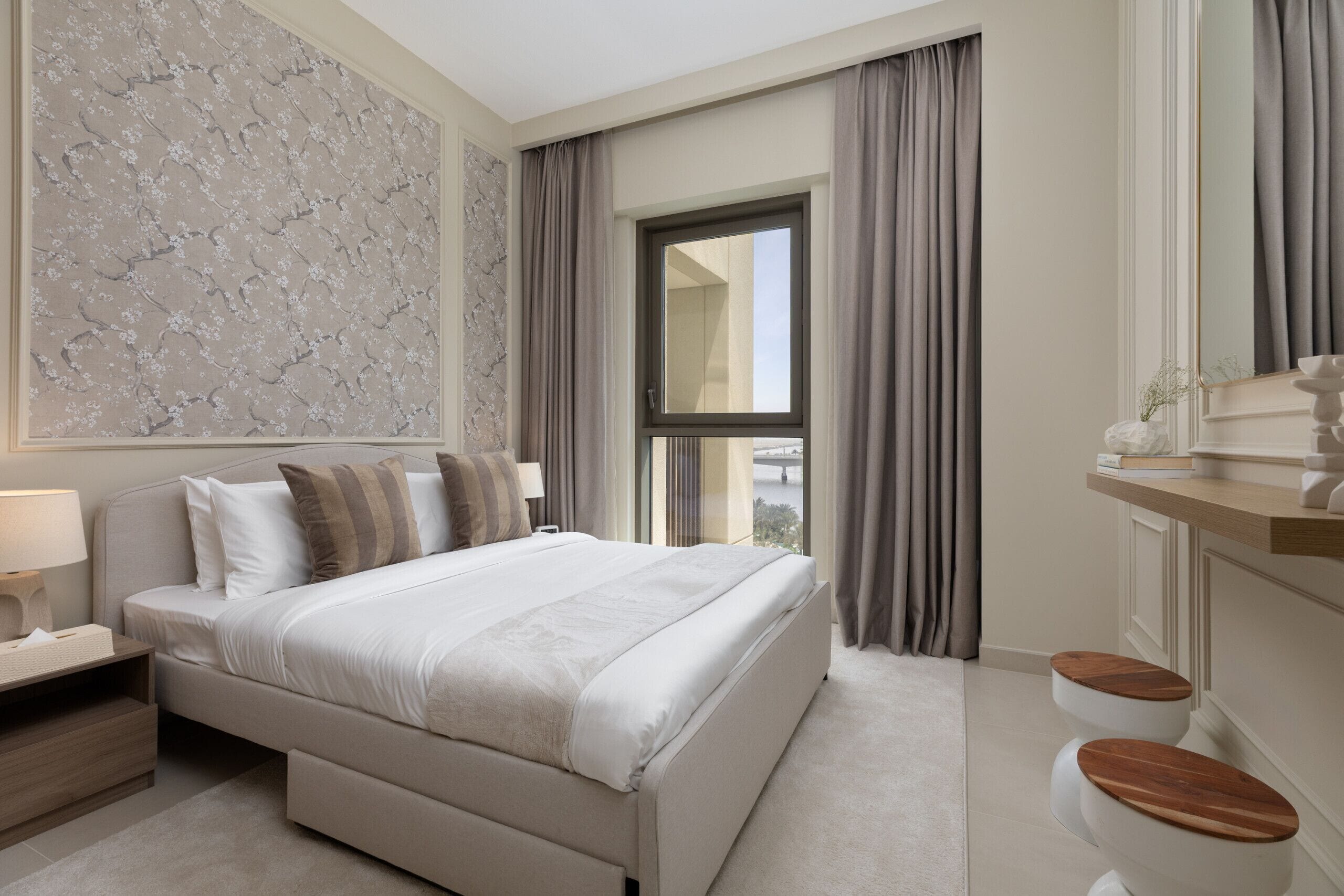 A modern bedroom with a large bed, a nightstand, a mirror, and a window with curtains.