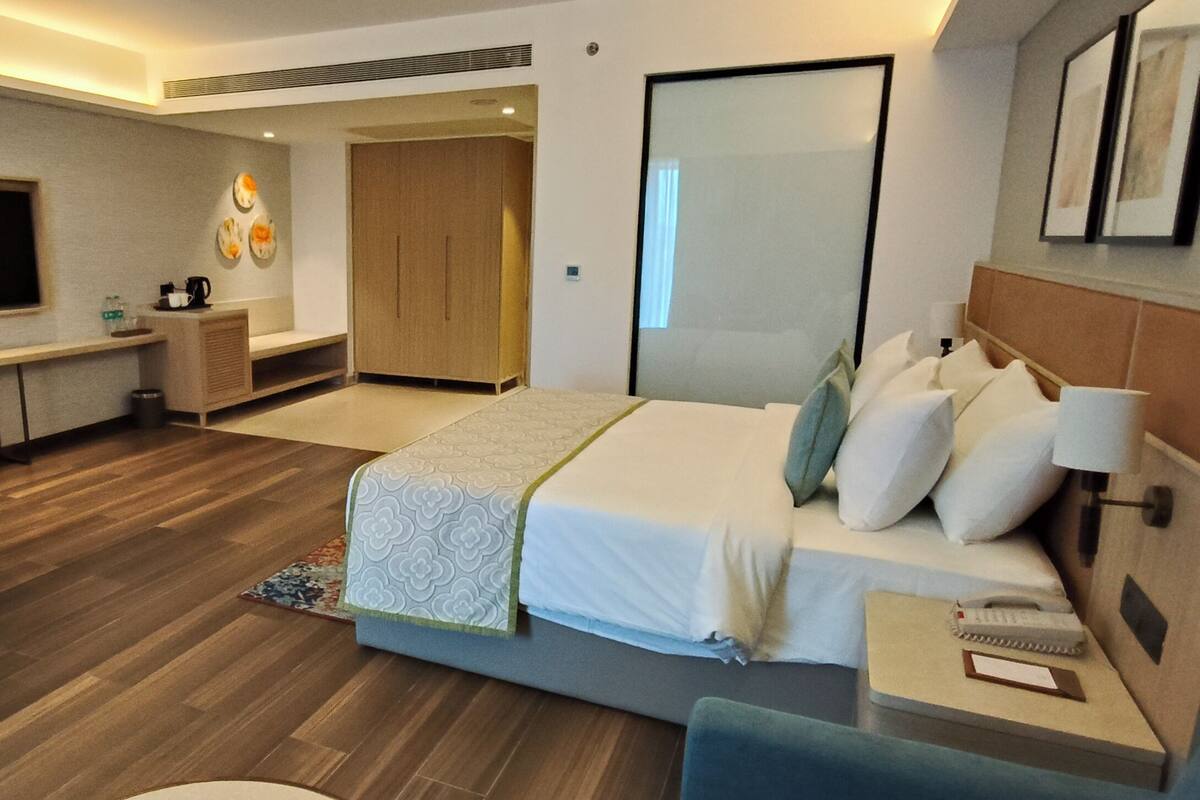 Ein Hotelzimmer mit Bett, Nachttisch, Lampe, Sessel, Schreibtisch, Fernseher und Kleiderschrank.