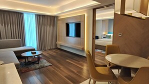 A modern hotel room with a sofa, a dining table with chairs, a TV mounted on the wall, and a large window with curtains. - Siddharth The Fern An Ecotel Hotel Jalna (Jalna)