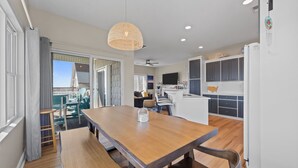 A modern kitchen with white cabinets, a central island, and a dining area with a wooden table and benches. - Steps to Beach Access, 4 Bedrooms w/ King Suite, Fenced Yard, Pup Friendly (North Topsail Beach)