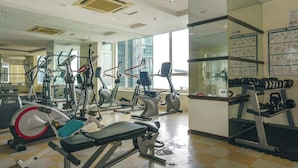 Une salle de sport équipée de divers appareils d’exercice, dotée d’un mur avec des miroirs et d’une fenêtre laissant entrer la lumière naturelle.