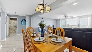 A dining area with a wooden table set for four, surrounded by wooden chairs. A blue vase with greenery is on the table.