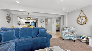 A living room with a blue sofa, a patterned armchair, and a dining area in the background.