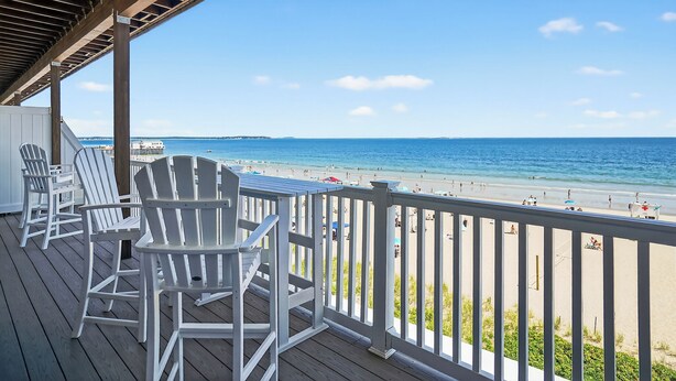 A wooden deck with Adirondack chairs overlooking a beach.