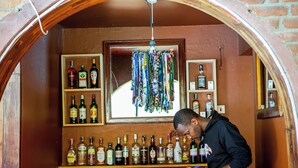 Zona de bar con estantes llenos de botellas de licores y una persona escribiendo en una mesa de madera.