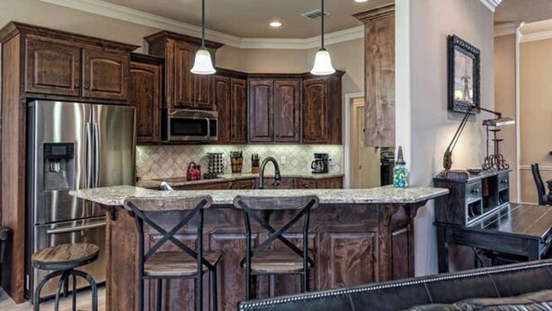 A kitchen with wooden cabinets, a stainless steel refrigerator, a microwave, and a large island with bar stools.