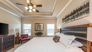 A spacious bedroom with a large bed, a ceiling fan, a television, and a red chair.