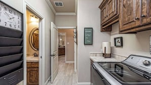 A kitchen with a clock, wooden cabinets, and a laundry area.