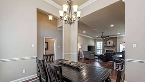 A dining area with a dark wooden table and chairs, a chandelier, and a fireplace in the background.