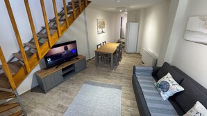 Un salon moderne avec un escalier en bois, un téléviseur à écran plat, un coin repas et un canapé agrémenté de coussins décoratifs.