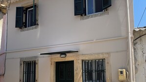 Un bâtiment à deux étages, doté d’une façade beige, d’une porte noire et de deux fenêtres avec des volets.