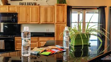 A kitchen with wooden cabinets, a microwave, a glass table with a plant and water bottles, and a laptop.