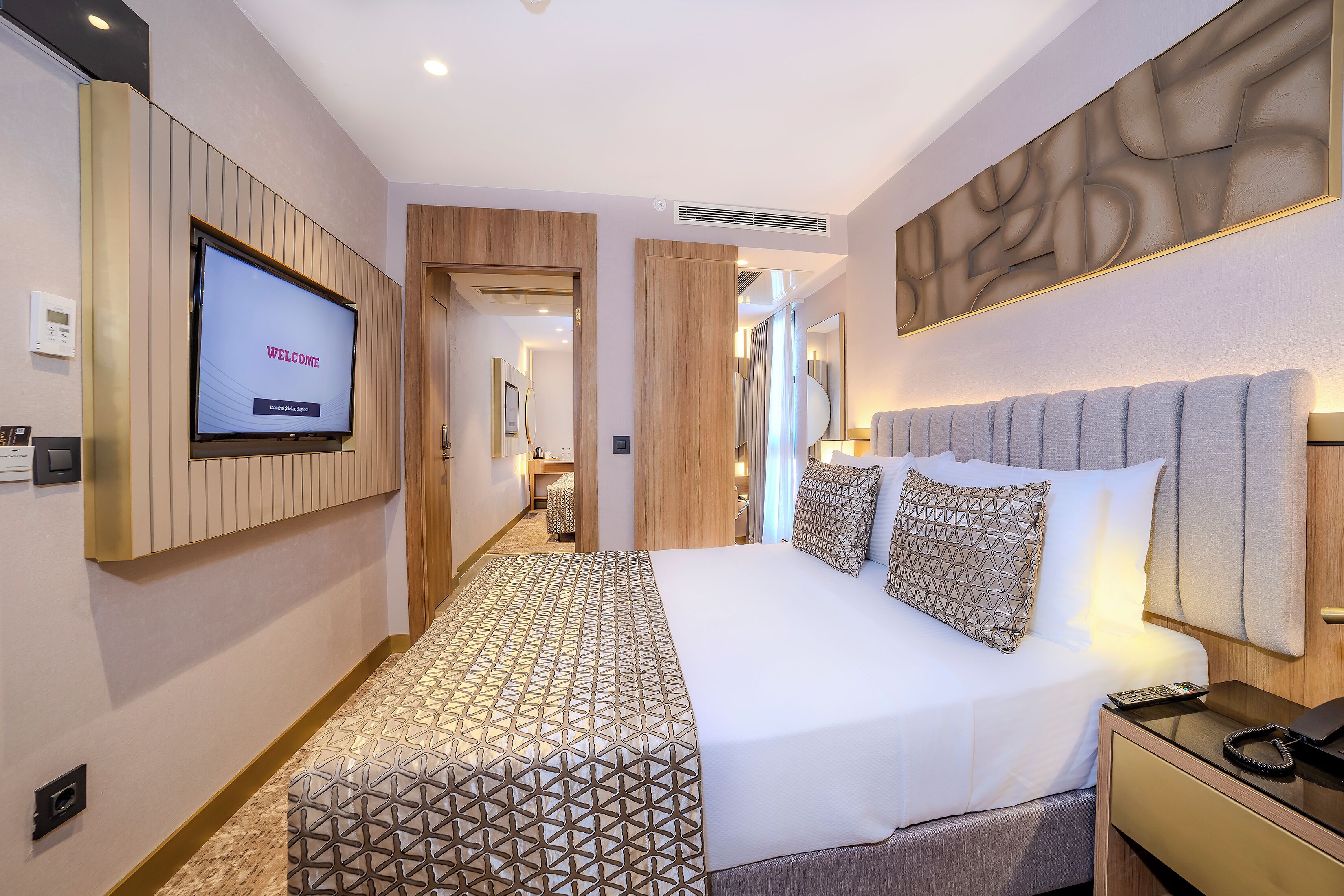 A modern hotel room with a large bed, a TV displaying "WELCOME", and a patterned carpet.