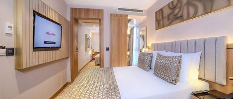 A modern hotel room with a large bed, a TV displaying "WELCOME", and a patterned carpet.