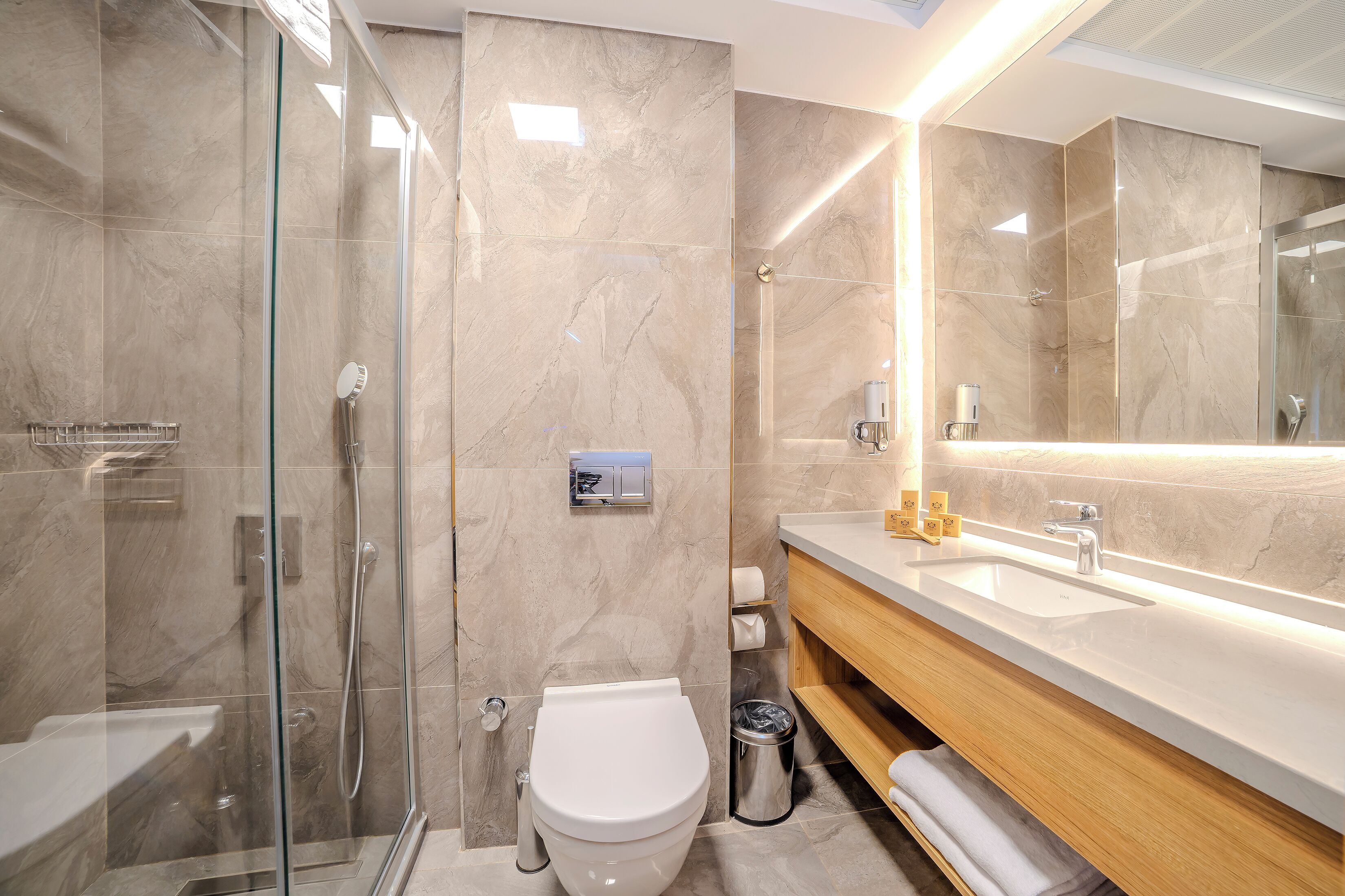 A modern bathroom with a glass-enclosed shower, a white toilet, and a wooden vanity with a sink.