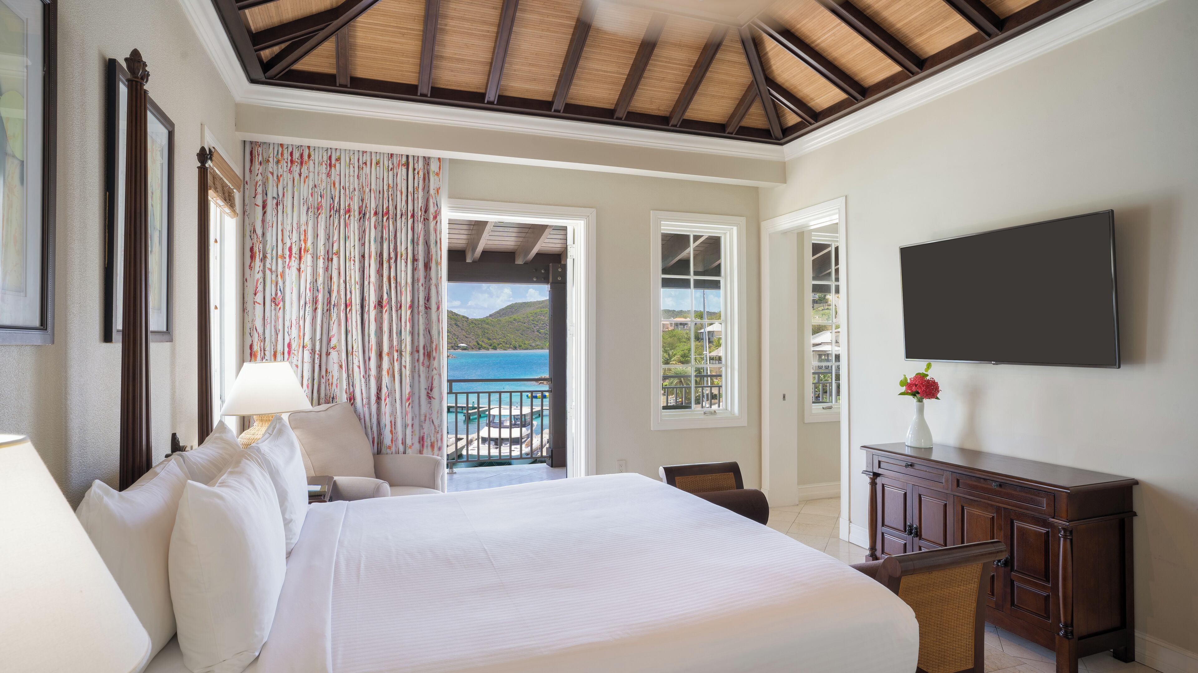 Une chambre d’hôtel avec un grand lit, un bureau, une télévision et un balcon donnant sur la mer.