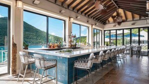 Zona de bar con una barra larga, varios taburetes y vistas a un paisaje montañoso a través de amplias ventanas.