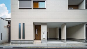 Un edificio moderno con fachada plana, dos paneles de vidrio verticales, una puerta de madera y una pequeña ventana con cortina.