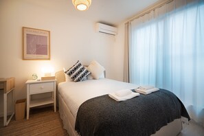 A hotel room with a bed, a nightstand, a framed artwork, and a window with curtains.