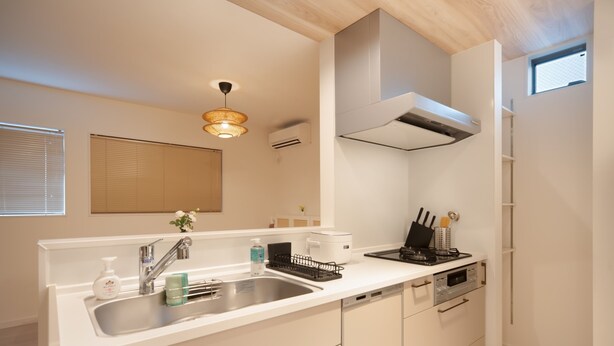 Una cocina moderna con encimera blanca, pileta de acero inoxidable y horno integrado. Se observa una ventana con persianas y una lámpara en el techo.