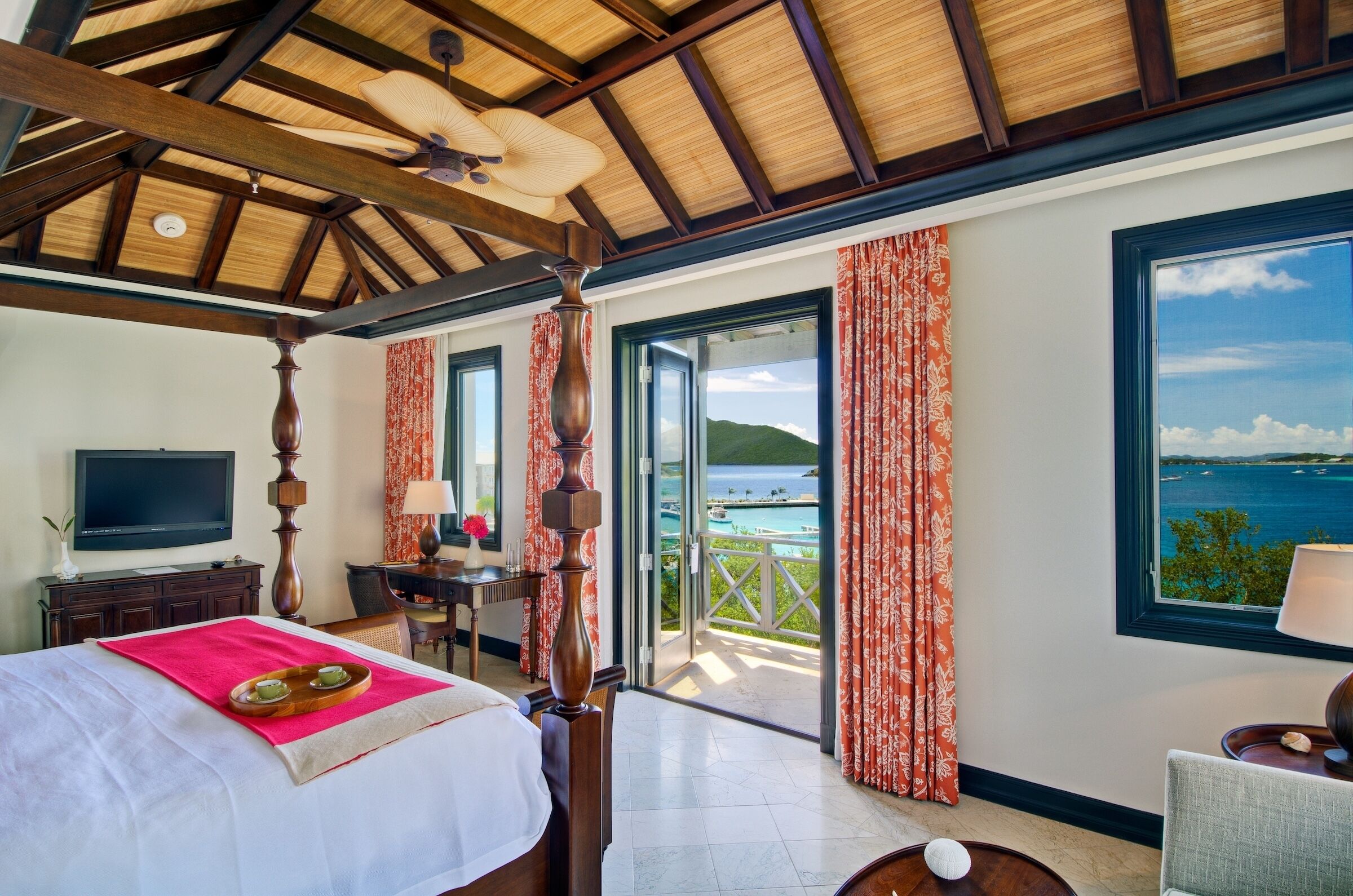 A hotel room with a bed, a TV, a desk, and a view of the sea.