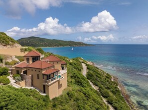 Eine Küstenvilla mit Pool, umgeben von üppiger Vegetation und freiem Blick auf das Meer.