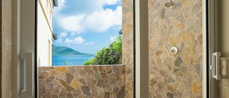 An open door revealing a stone wall and a view of a body of water with a mountain in the distance.