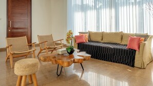 Una sala de estar con un sofá, dos sillas de madera, una mesa de centro y una puerta.