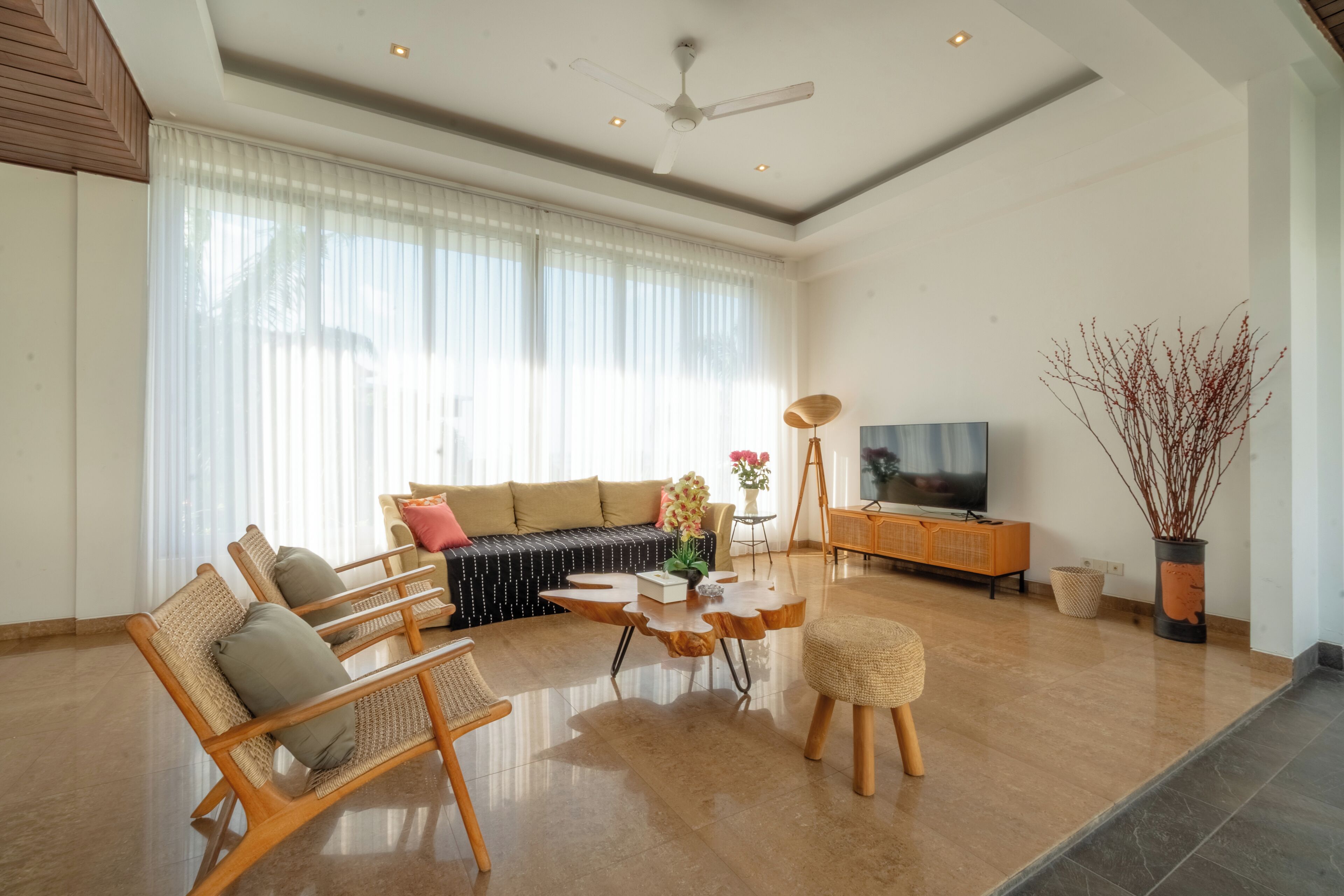 A spacious living room with a large sofa, wooden chairs, a coffee table, and a television.