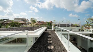 Una terraza en la azotea con un camino de grava, barandas de vidrio y vistas de edificios circundantes.
