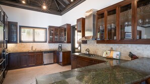 Una cocina moderna con alacenas de madera oscura, una isla grande con encimera de granito, electrodomésticos de acero inoxidable y vistas al exterior a través de una ventana.