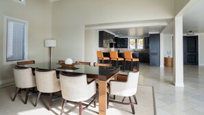 Un comedor espacioso con una mesa de vidrio rodeada de sillas, una cocina al fondo y vistas al exterior.