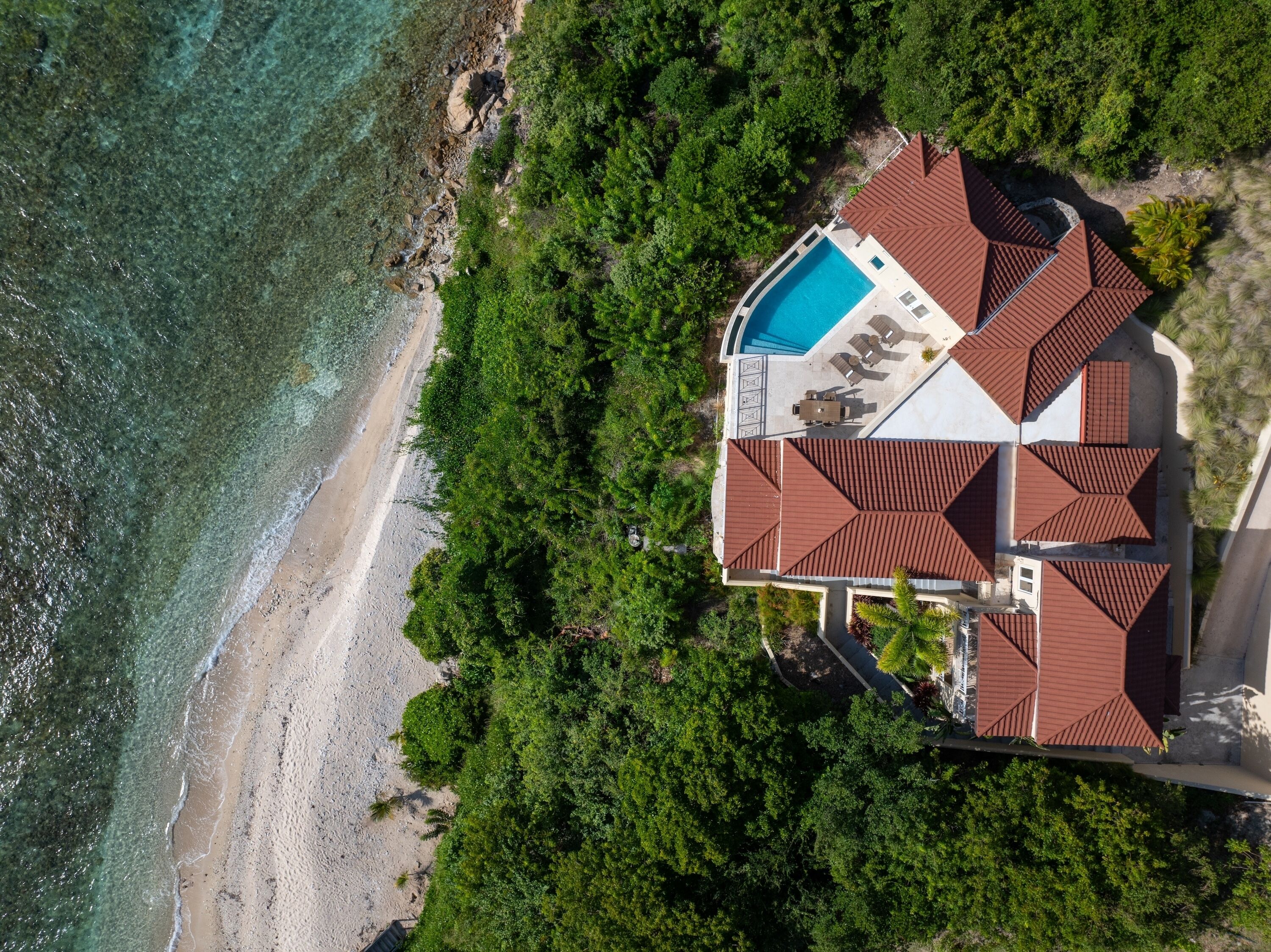 Vista aerea di una casa con piscina, immersa in vegetazione lussureggiante e affacciata su una spiaggia.