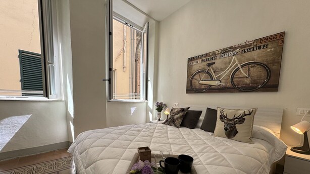 A bedroom with a large bed, a window with blinds, a wall-mounted bicycle poster, and a bedside table with a lamp. - Nice apartment for 5 guests with WIFI, A/C and TV (Lucca)