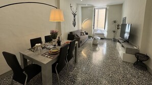 A modern living room with a dining area, a sofa, a TV, and a large window. - Nice apartment for 5 guests with WIFI, A/C and TV (Lucca)