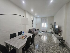 A modern living room with a dining area, a sofa, a TV, and a decorative wall piece.