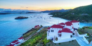 A coastal property with a white building featuring red roofs, a beach with sailboats, and a mountainous backdrop.